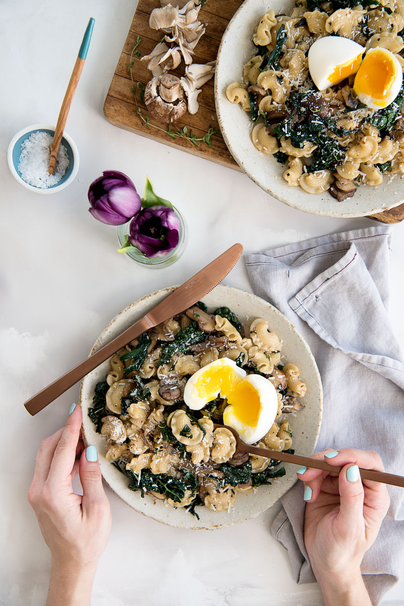 Marble background with a a mushroom, pasta dish, side napkin and a flower in the top left corner. 